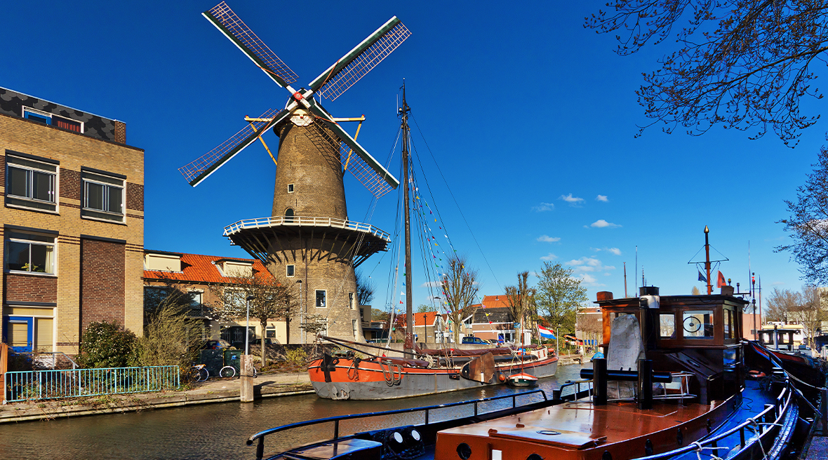 Windmill in background on bank of a canal, with canal boats and barges in the foreground. Cloudless deep blue sky